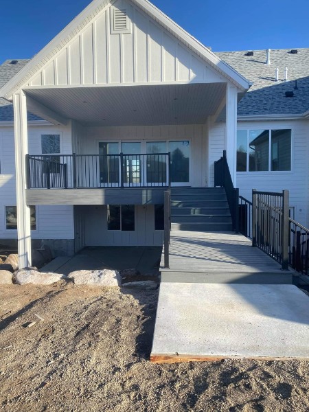 Covered composite deck with stairs and a sloped approach beside a home