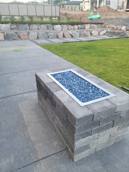 Fire-feature detail with blue glass, lawn and boulder retaining context.