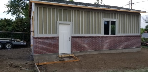 Garage side wall with pale siding, a red brick base and service door.