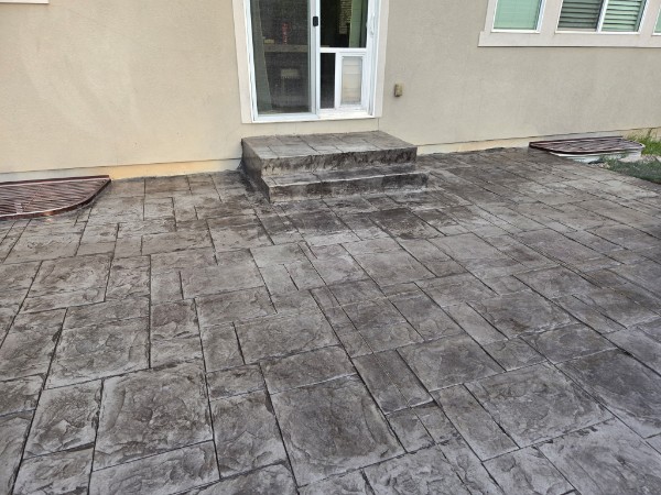 Stamped concrete patio and two-step entry beside a tan stucco house.